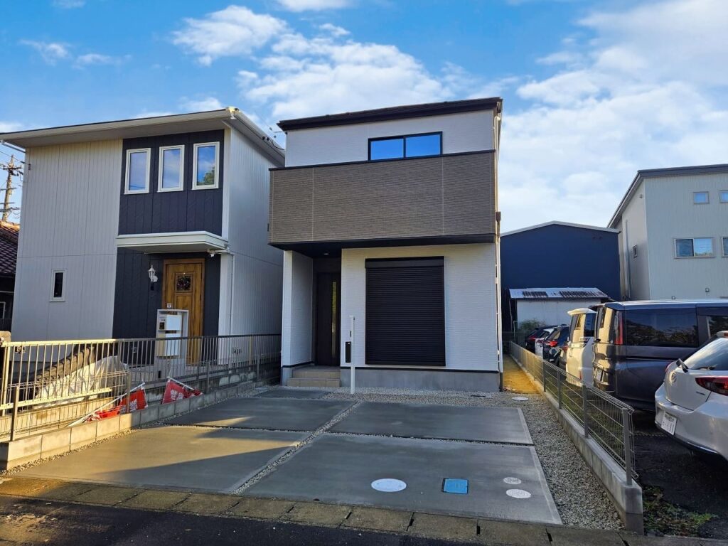 稲沢市小池一丁目の新築一戸建て完成後外観写真。落ち着いた色合いの外壁とバルコニーデザインが印象的。並列駐車2台分のスペースを確保したゆとりある配置。