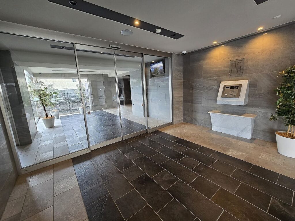ロフティ稲沢駅前の高級感あふれるエントランスホール。大理石調の床材と壁面、自動ドア、オートロックシステム、モニター付きインターホンを完備した洗練された共用空間。