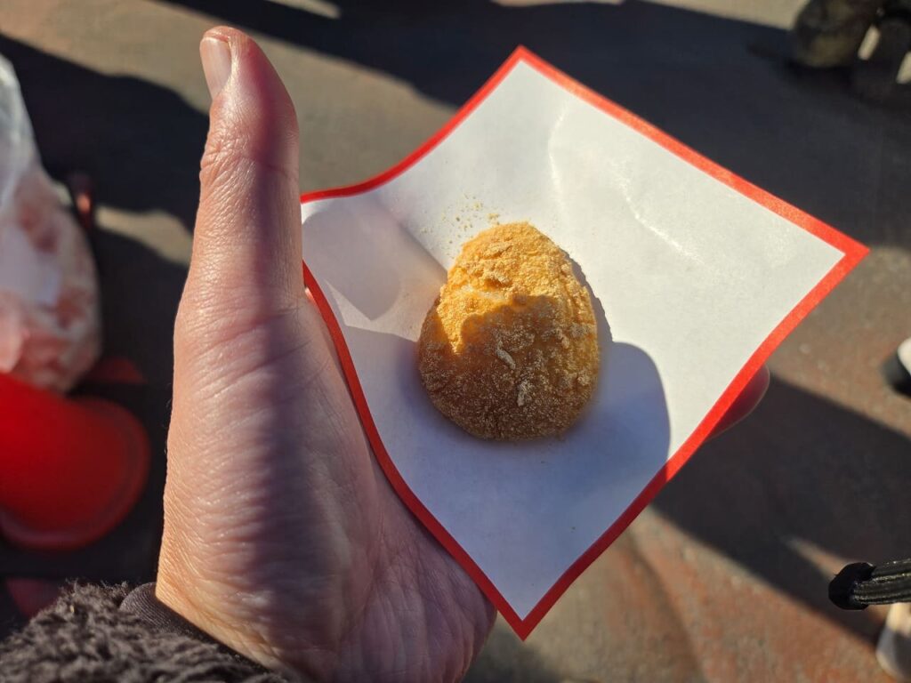 国府宮神社で配布された福餅を手に持っている写真。白と赤の紙の上に、きな粉がまぶされた丸いお餅が一つ乗っている。