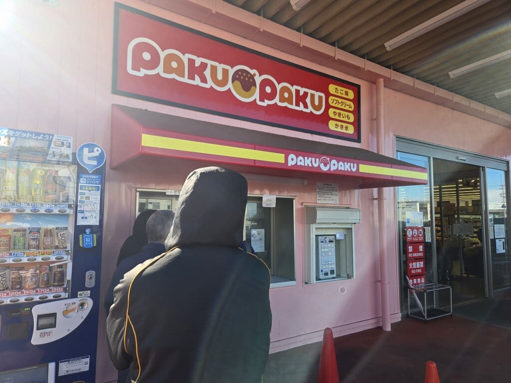 ラ・ムー稲沢店に併設された赤い看板が目印の100円ファストフード店「PAKUPAKU（パクパク）」。窓口の横には食券用の券売機があり、購入待ちの行列ができている様子。