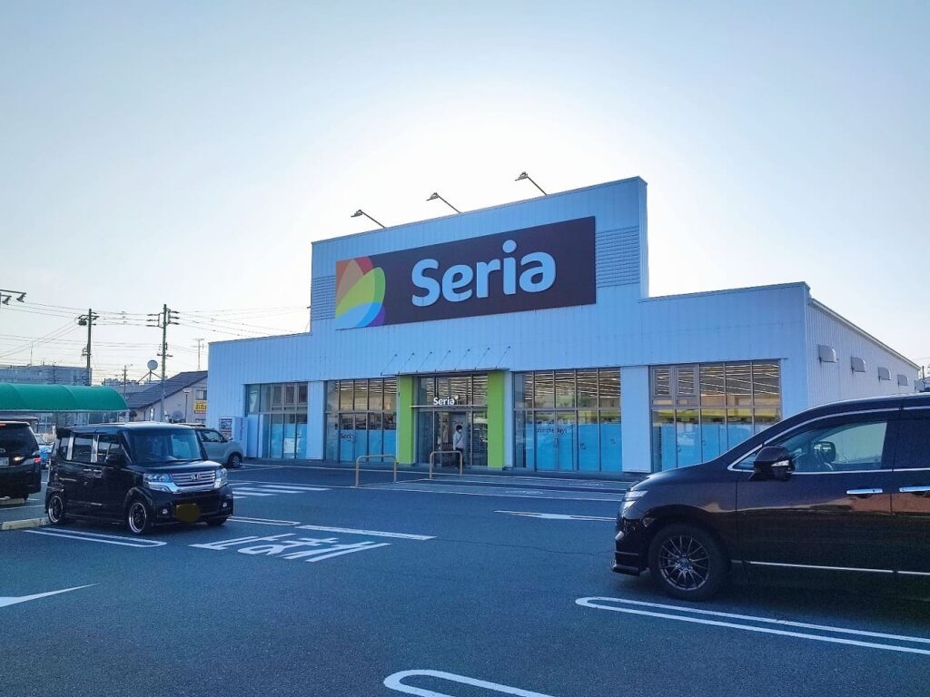 ニッケタウン稲沢のSeria(セリア)の外観。青い建物に大きなSeriaのロゴマークとカラフルな緑のアクセントが特徴的な100円均一ショップ。駐車場には複数の車両が停車し、手軽に買い物ができる利便性の高い立地