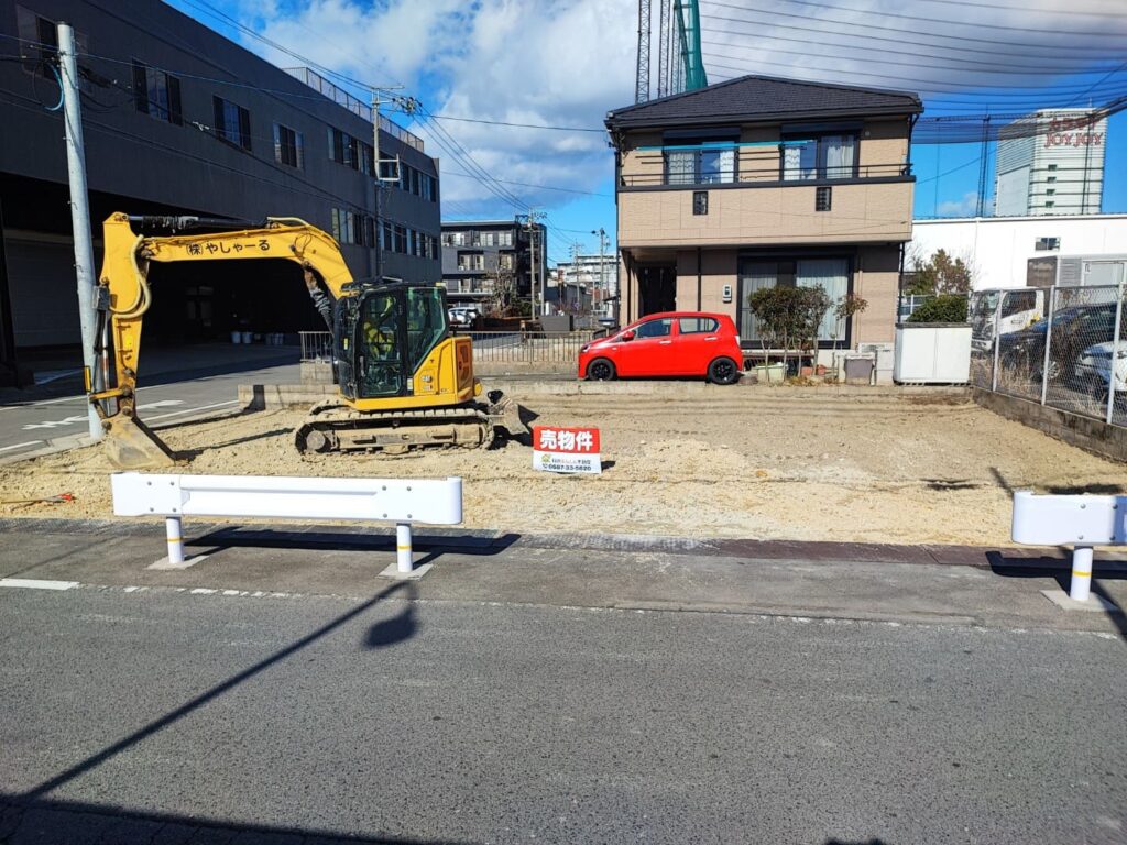 稲沢市奥田大沢町にある売地の現地写真。南側道路に面した更地で、敷地内には重機が入り整地作業が行われている様子。前面道路は幅があり、住宅や商業施設が周囲に立ち並ぶエリア。