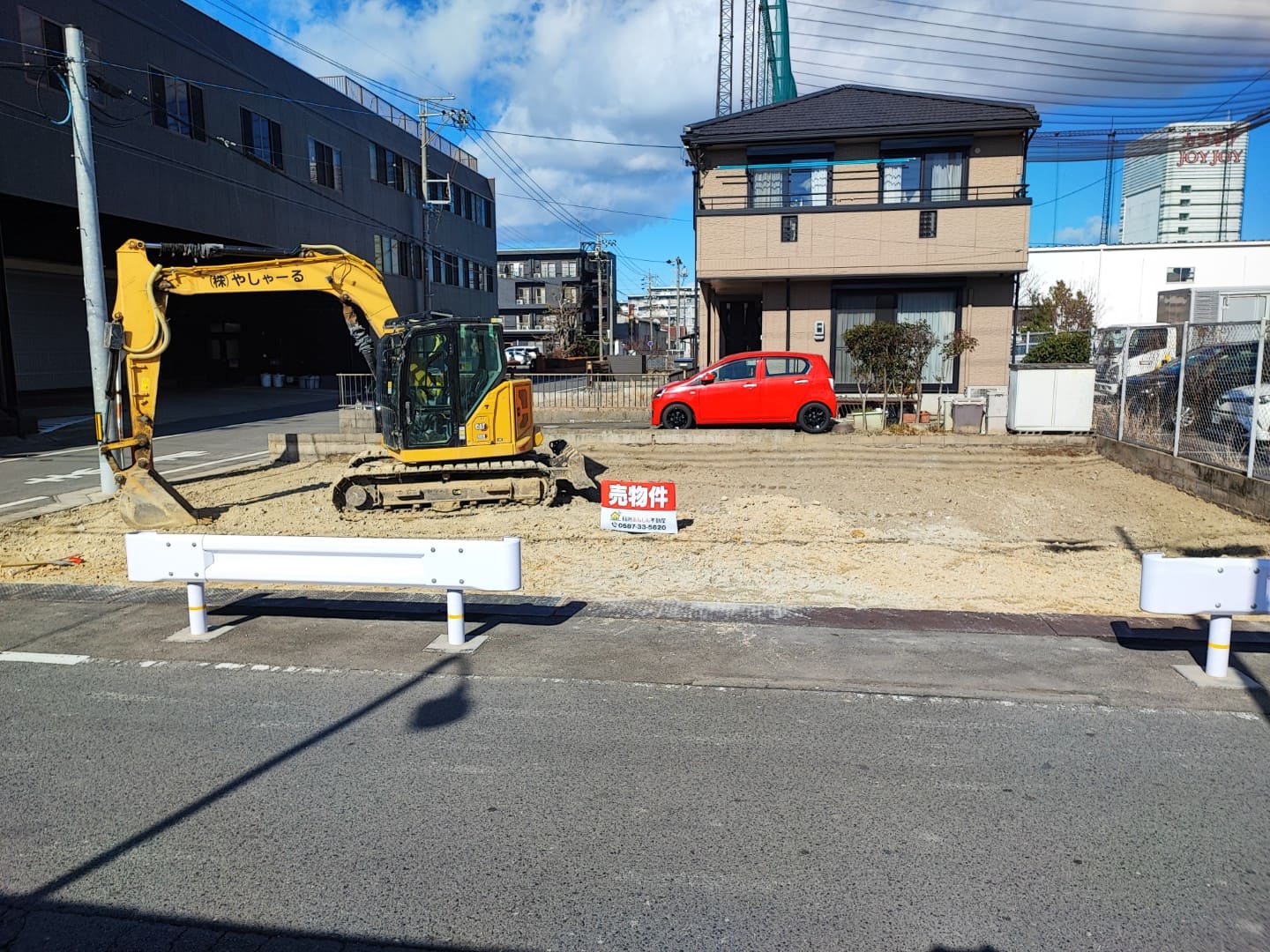 稲沢市奥田大沢町にある売地の現地写真。南側道路に面した更地で、敷地内には重機が入り整地作業が行われている様子。前面道路は幅があり、住宅や商業施設が周囲に立ち並ぶエリア。