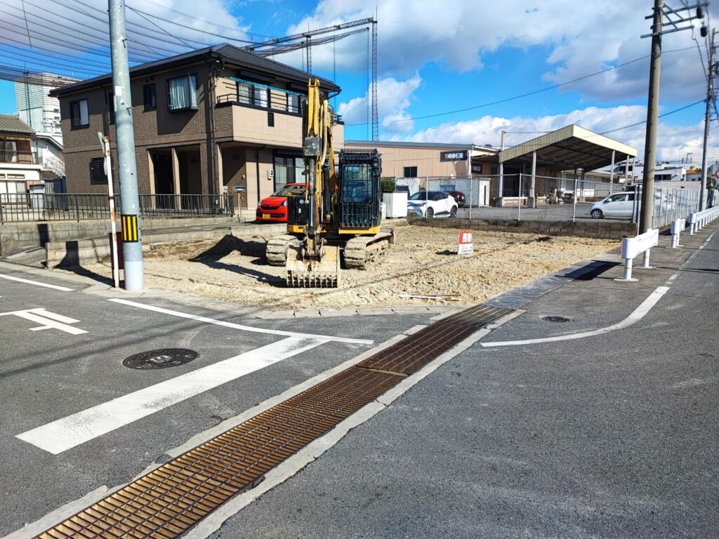 愛知県稲沢市奥田大沢町の売地現地写真。角地に位置する更地で、前面道路は幅員があり交差点に面している。敷地内には重機が入り、整地が進められている様子が確認できる。