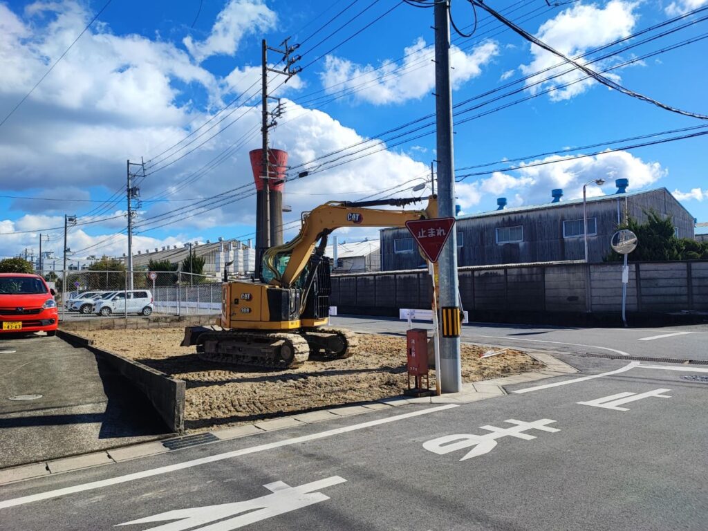 愛知県稲沢市奥田大沢町にある売地の現地写真。交差点に面した角地で、整地された敷地内に重機が置かれている。周囲は工場や住宅が立ち並び、前面道路の見通しが良い立地。