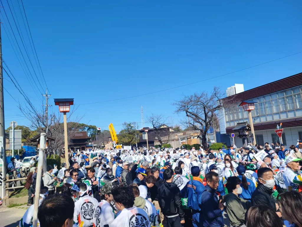 国府宮神社の参道に集まる大勢の参拝客と祭り関係者。白い法被を着た「はだか祭」の参加者や、青い制服の消防団が密集しており、奥には黄色いクレーン車が見える活気ある境内の風景。