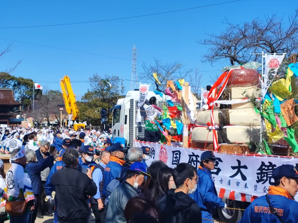 「国府宮大鏡」と書かれた横断幕が掲げられたトラックの荷台。積み上げられた巨大な白い餅には、赤い飾り紐や黒い昆布が巻かれ、周囲には願い事が書かれたカラフルな「なおいぎれ」が結び付けられている。