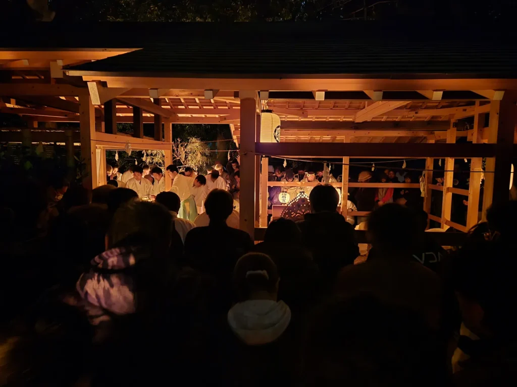 国府宮はだか祭・夜儺追神事。深夜3時、境内東南の庁舎（ちょうや）にほのかな明かりが灯り、白装束の神職たちが祝詞を奏上している。庁舎の周囲には参拝者が集まり、神楽の音が静寂の境内に響く