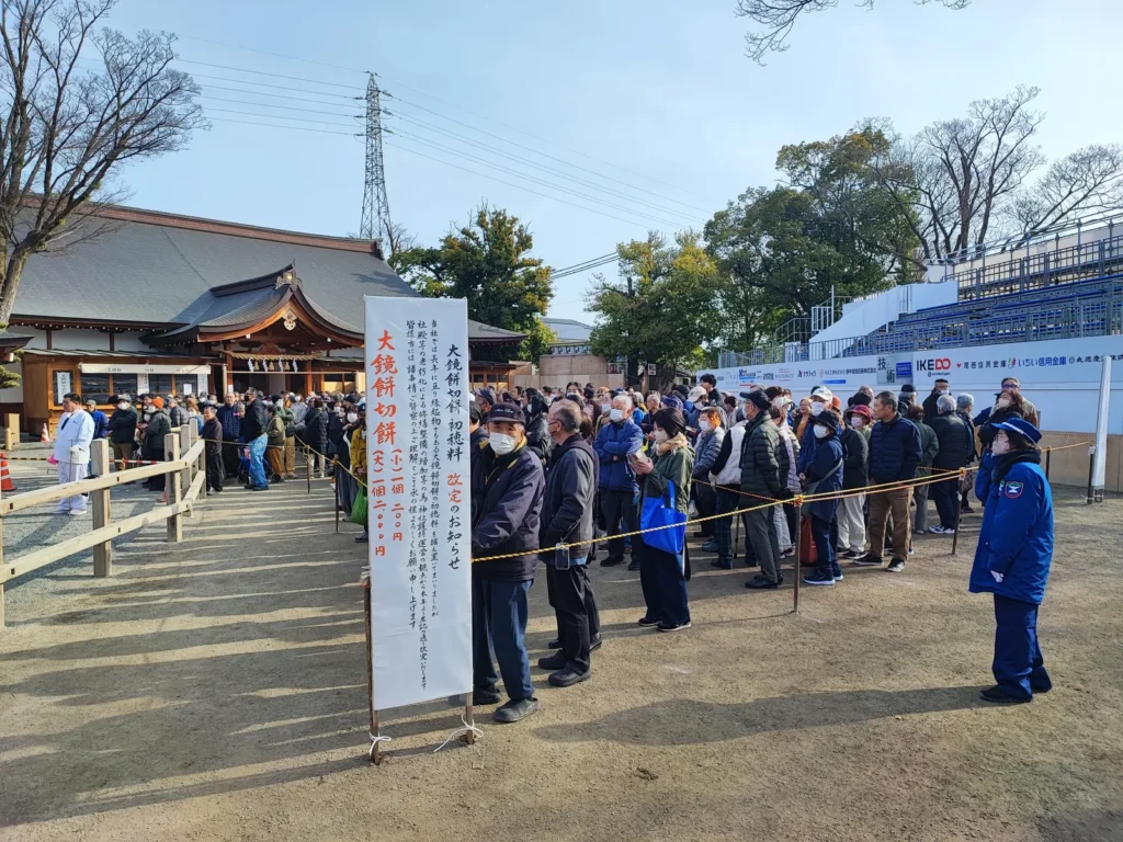 国府宮神社の大鏡餅餅切始の行列の様子。午前8時の開始直後から多くの参拝者が並び、長蛇の列ができている。手前には「大鏡餅切餅 2個200円」と書かれた看板が立っている。