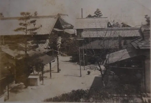 昭和初期に撮影されたセピア色の白黒写真。瓦屋根の日本家屋が数棟並び、手前には葉の落ちた木立と物干し竿、奥には煙突らしき突起が見える、当時の起宿周辺の町並みを写した古写真。