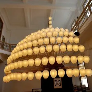 津島市観光交流センターの館内に展示されている、尾張津島天王祭の宵祭を再現した半円形・扇状の実物大提灯。淡い黄色の提灯が幾重にも連なり、天井近くから吊り下げられて温かい光を放っている。手前には奉納品を置く台が見える。