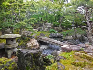旧林氏庭園の一角。苔むした庭石と石灯籠、小さな石橋が配された池の周りを、赤松や庭木が取り囲む、静かな回遊式日本庭園の風景。