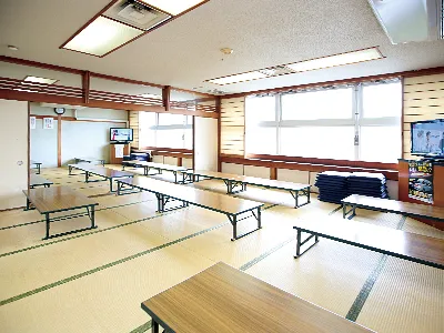 羽島温泉の畳敷きの休憩室。木製の座卓が数台並び、奥にはテレビと大きな窓があり、右手には飲み物の自動販売機が設置されている。人物は写っていない。