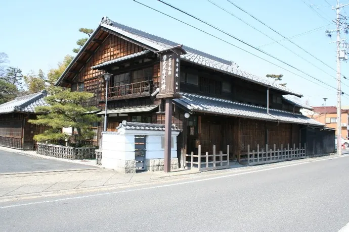起宿の街道沿いに建つ旧林家住宅の外観。黒い瓦屋根と焦げ茶色の格子窓を持つ木造二階建ての町家に、白壁の土蔵と松の木が寄り添い、玄関脇に「一宮市尾西歴史民俗資料館」の看板が立てられている。
