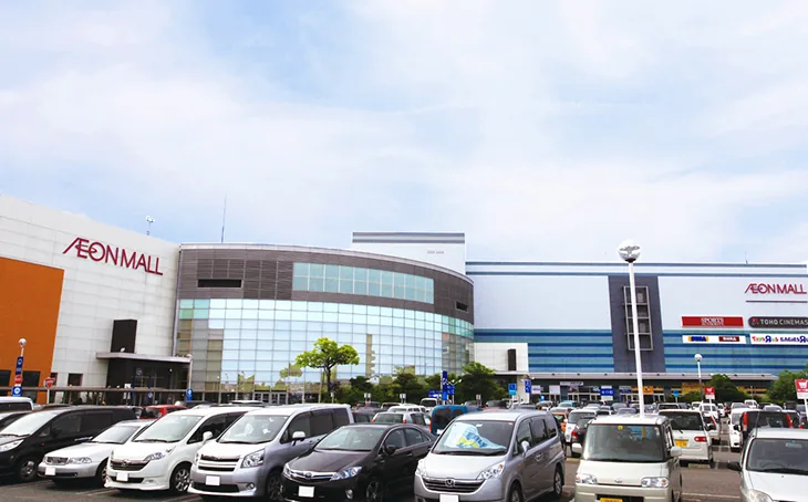 イオンモール木曽川の外観。青空の下、白い外壁にAEON MALLのロゴが掲げられた建物正面と、TOHOシネマズやスポーツ用品店の看板が並ぶ。手前には広い平面駐車場に多数の乗用車が停まっており、買い物客の姿は写っていない。