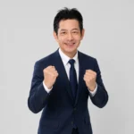 稲沢あんしん不動産 代表 佐藤高樹が両手で拳を握り、前を向いて意気込んでいる写真。売却のご相談に全力で取り組む姿勢を表す、会社概要ページの締めくくりの一枚。相談・査定は無料であることを伝える案内のとなりに置いている。