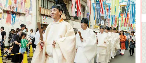 御衣奉献大行列の様子。白い装束に烏帽子姿の神職らが笏を手に列をなし、色とりどりの七夕飾りの吹き流しが揺れる本町商店街を厳かに進んでいる。沿道では大勢の見物客が行列を見守っている。