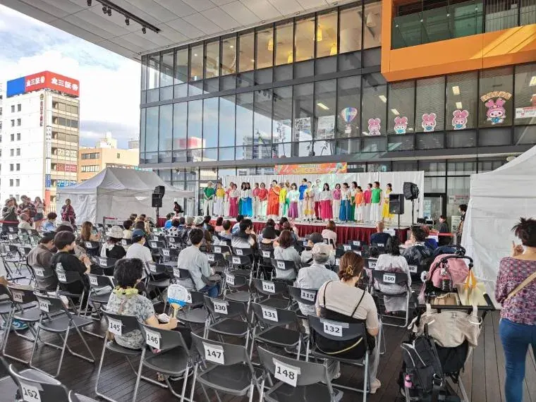 七夕ステージの様子。ステージ上で衣装をそろえた出演者たちがダンスパフォーマンスを披露し、大勢の観客が見守っている。2026年は熱中症対策のため会場が屋内のi-ビル7階シビックホールに変わる。