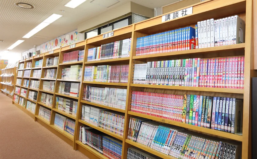 稲沢市立平和町図書館の館内、天井近くまで届く木製書棚にコミック(漫画)の背表紙がぎっしりと並ぶ書架の様子。蔵書量の多さが伝わる構図。