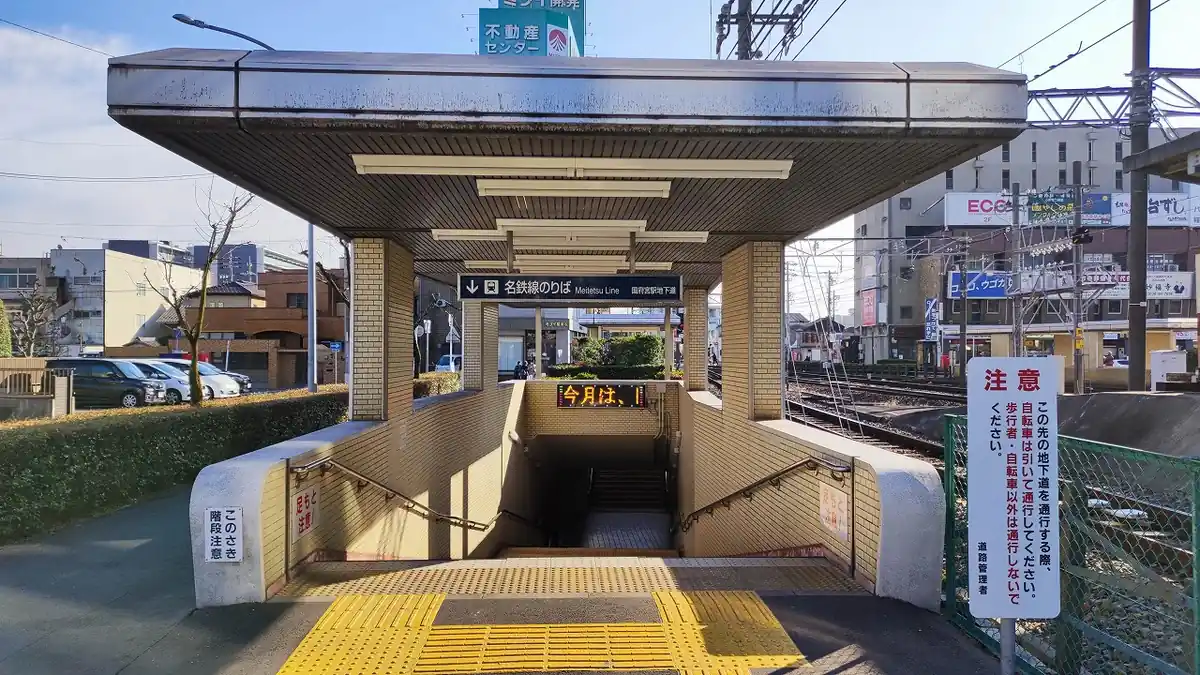 国府宮駅地下道の入口階段。「名鉄線のりば」の案内板が掲げられ、屋根付きの階段が地下改札へ下りていく様子。