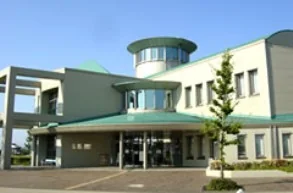 祖父江の森図書館の建物外観。白とベージュを基調とした2階建ての公共施設で、右手前に円柱形のガラス張りの塔状部分が見える。