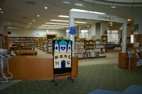 祖父江の森図書館の児童開架室。カラフルな「おはなし会」の案内ボードと絵本の書架が並ぶ、子ども向けの読書スペース。