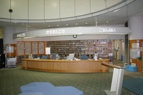 祖父江の森図書館の受付カウンター。木目調の曲線を描くカウンターに「かりるところ」「ごあんない」の案内サインが掲げられている。