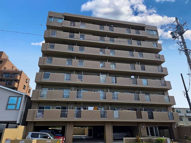 藤和シティコープ国府宮Ⅱの正面外観。整然としたバルコニーが特徴のマンションで、1階部分には駐車場があり、晴天のもとで撮影されている。