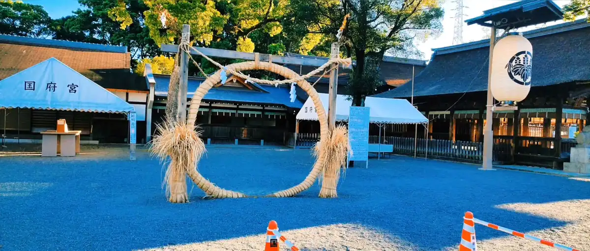 国府宮神社の拝殿前に設置された大きな茅の輪。左右の注連縄と紙垂、国府宮の白いテント、右側の提灯が写っている。2023年8月11日撮影の動画から切り出し。
