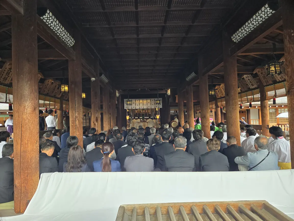 国府宮神社の拝殿内部で御田植祭の祭典を見守る多数の参列者。正面に祭壇と白い幕、左右に木の柱と灯りがあり、厳かな神事の様子が写っている。2026年6月28日撮影。